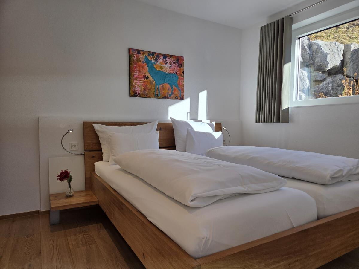 Zweites Schlafzimmer mit Doppelbett und Fenster zur Felswand in der Garten-Luxuslodge Hammerspitze, Luxuslodge für 6 Personen im Kleinwalsertal