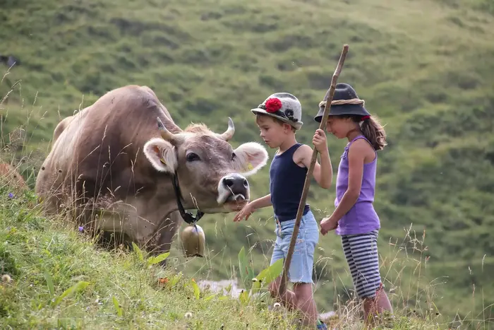 Zwei Kinder streicheln eine Kuh mit Glocke auf der Bergwiese