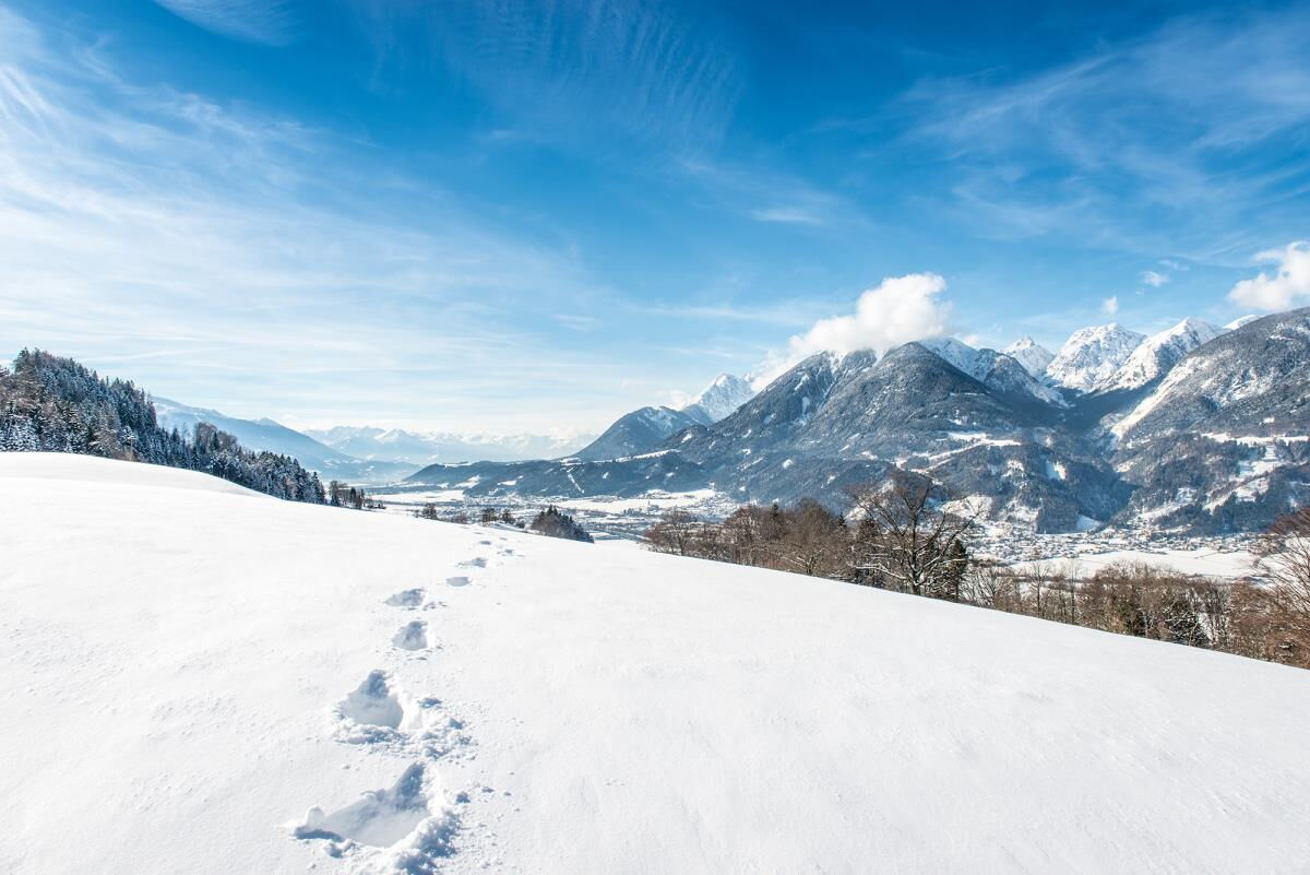 Schneeschuhspuren auf der weiten verschneiten Fläche am Kolsassberg mit Blick auf die Berge, Winterwandern ab der Ferienwohnung Sternenhimmel