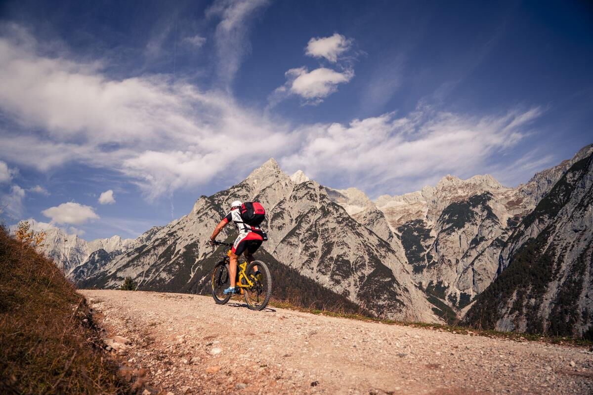Mountainbiker auf dem Schotterweg vor der mächtigen Felswand des Karwendelgebirges, Radtour ab der Pferdeheimat am Karwendel in Gnadenwald