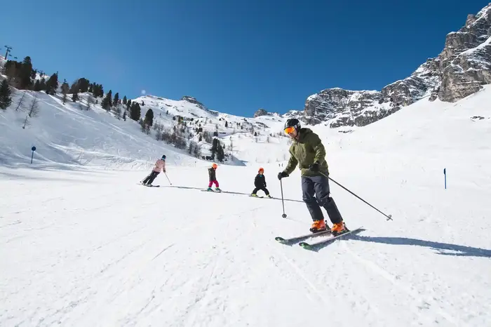 A skier on the wide sunlit piste below the rock faces