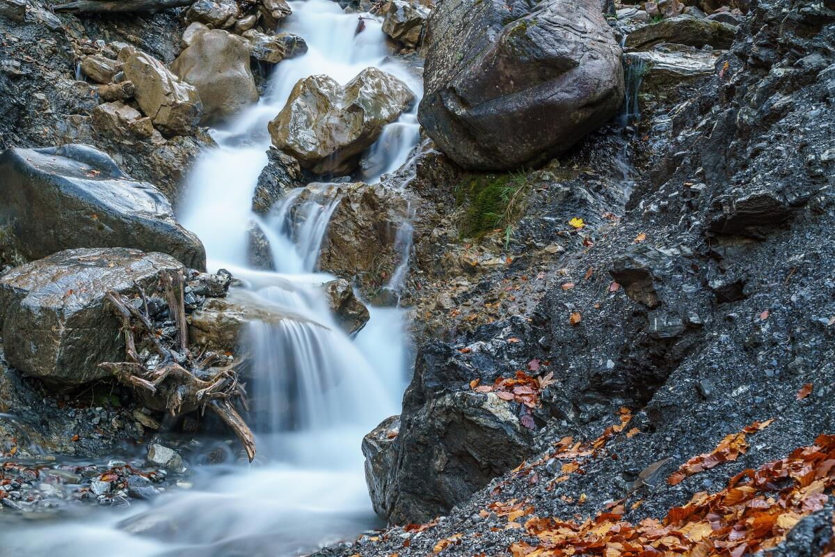 Waterfall tumbling over dark rock between colourful autumn leaves in the Kleinwalsertal