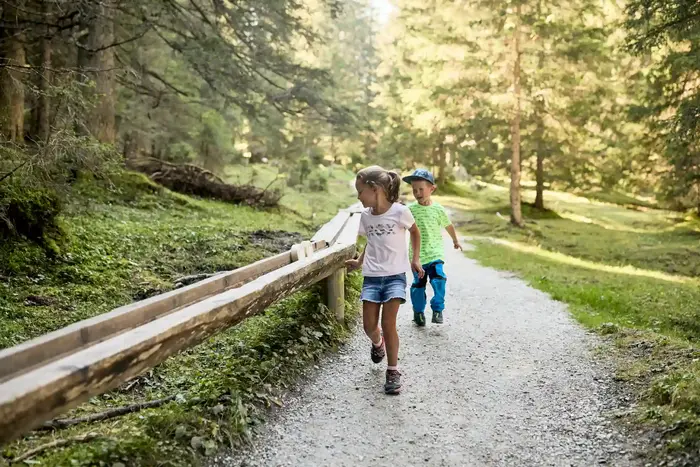 Two children walking the themed trail beside the wooden water channel through the forest
