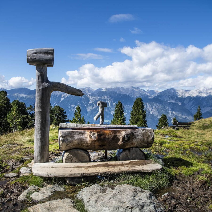 Der Zirbenweg in Tulfes mit Brunnen im Bildund im Hintergrund das Karwendel.