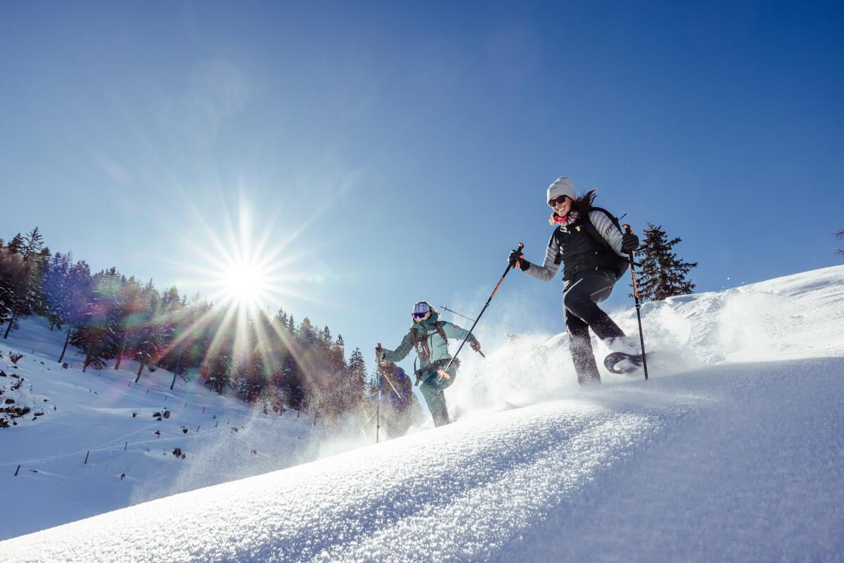 Zwei Skitourengeher steigen im Gegenlicht durch den Tiefschnee auf, Skitouren rund um die Roggnkammer am Riedhof in Breitenbach