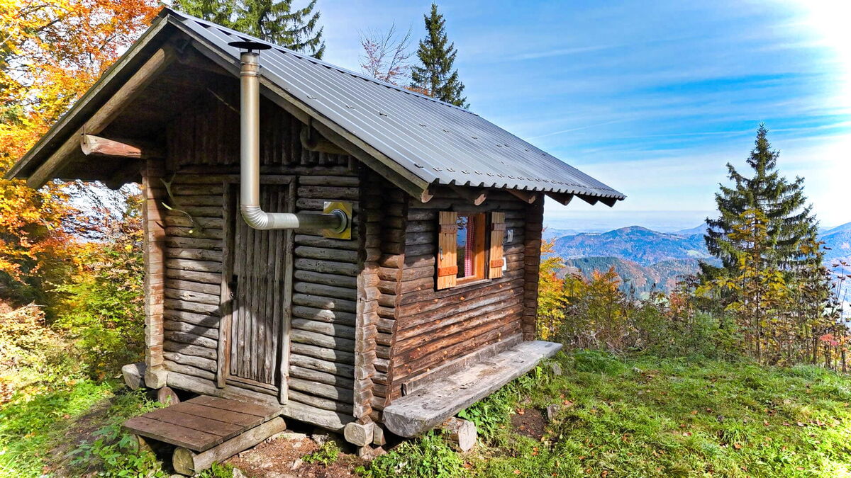 Seitenansicht der Abenteurer-Hütte mit verwitterter Holzfassade im herbstlichen Bergwald, Niederösterreich.