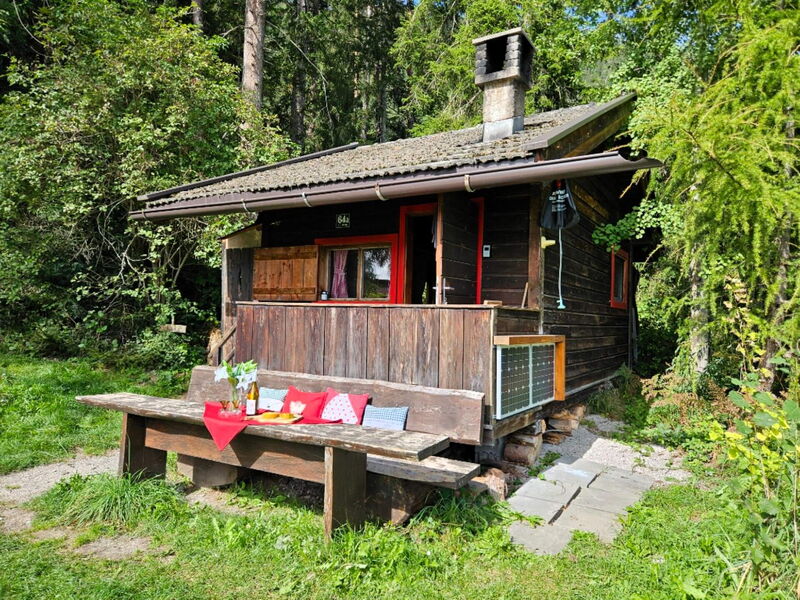 Side view of the Waldhüttl in Terfens with a weathered wooden bench by the door and a summer meadow.