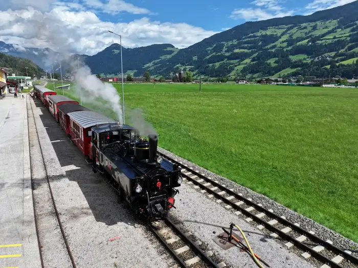 Steam train of the Zillertalbahn passing green meadows through the Zillertal
