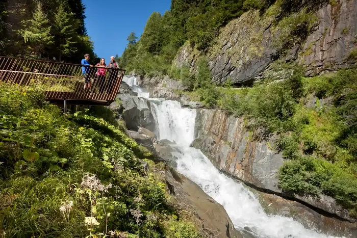 Drei Personen auf einer hölzernen Aussichtsplattform über einem Wasserfall in einer Klamm in Osttirol