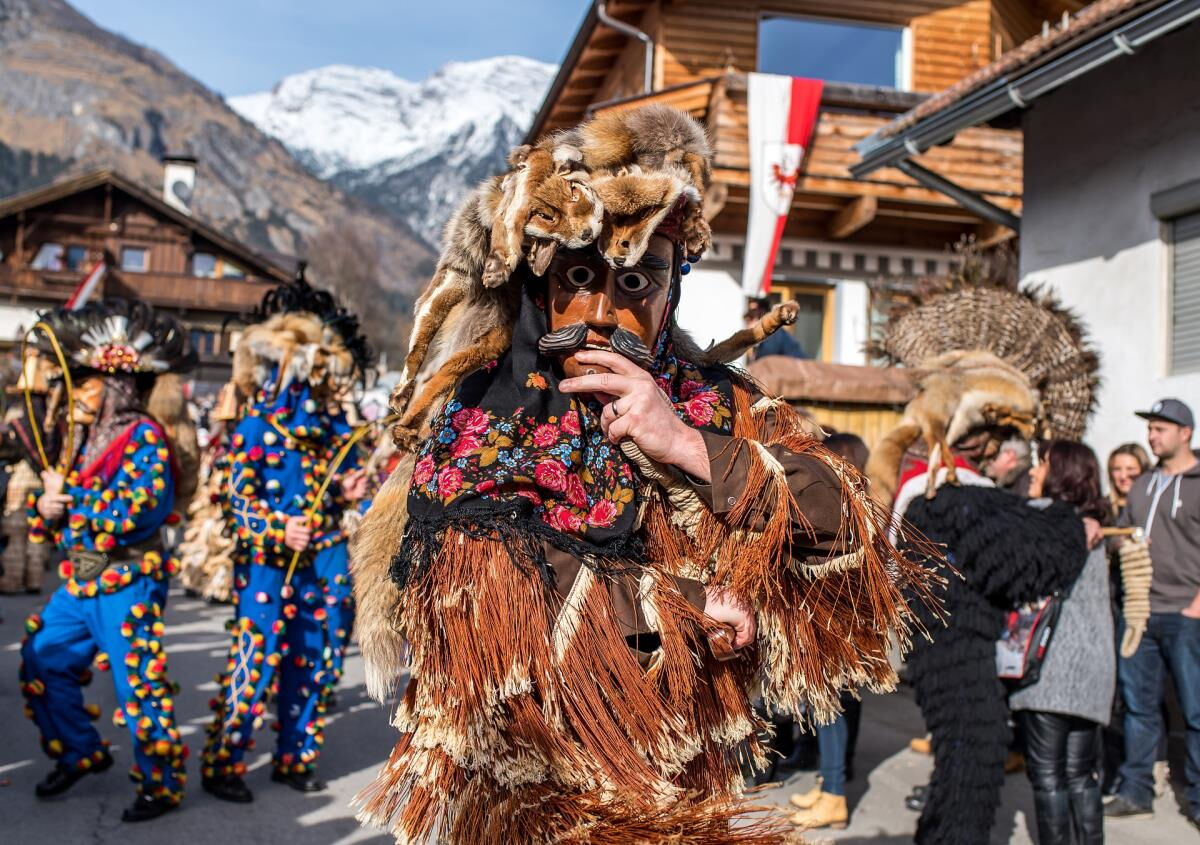 Maskierte Gestalten und Musikanten ziehen bei einem Tiroler Fasnachtsumzug durch den Ort