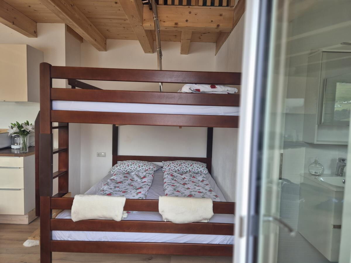 Stockbett aus Holz unter dem Dachstuhl der Ferienwohnung Sternenhimmel am Kolsassberg, vom Bett aus geht der Blick auf die Berge
