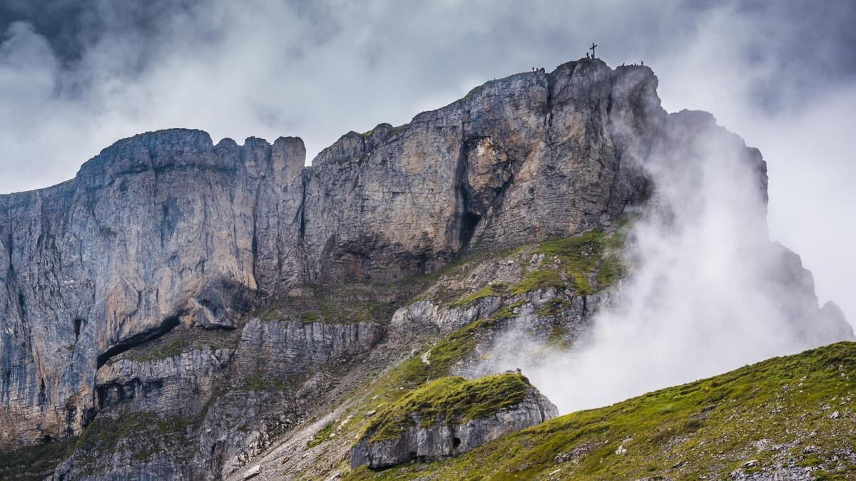Summit cross on a steep rock face wreathed in rising mist in the mountains of the Kleinwalsertal