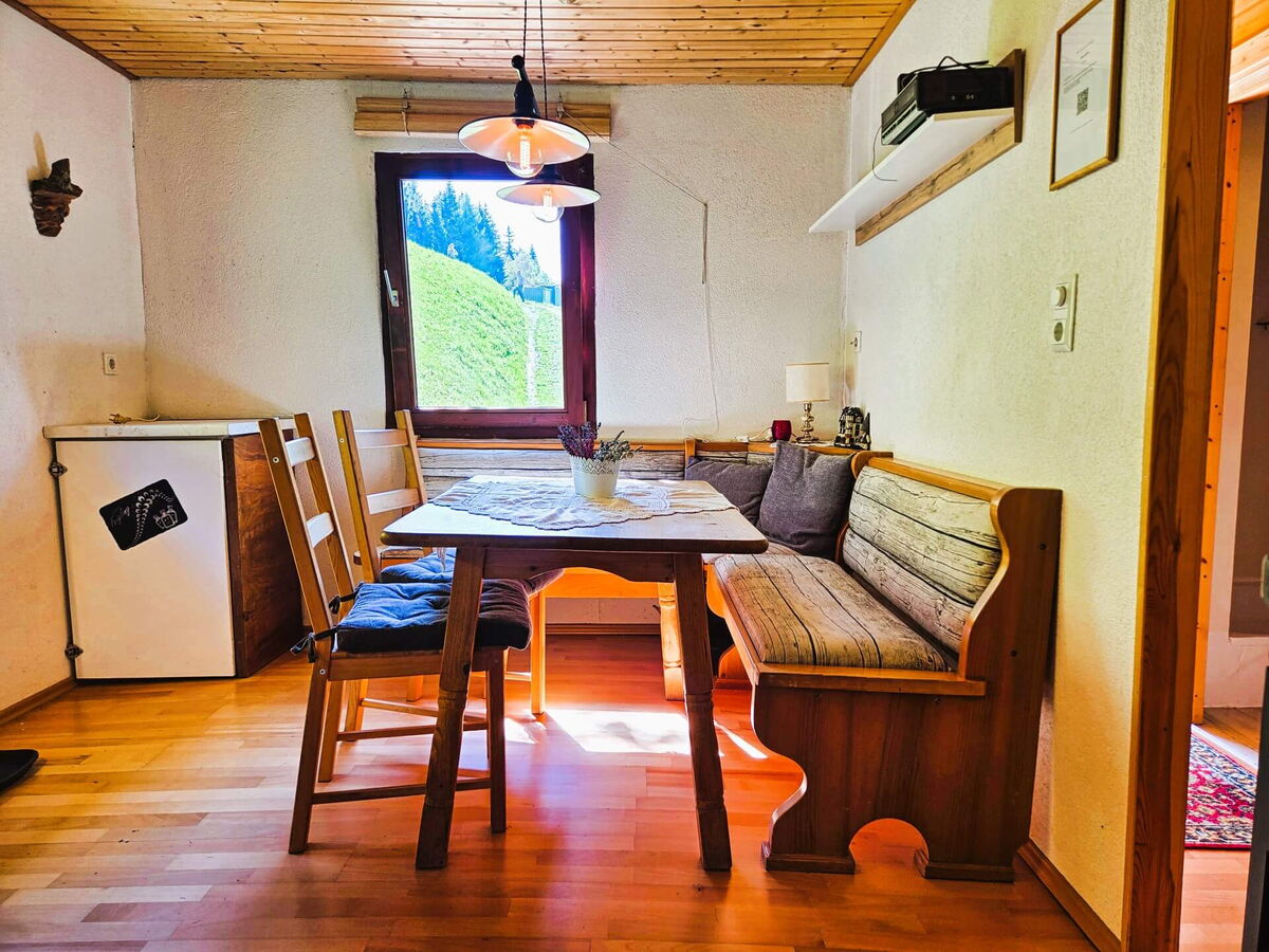 Essbereich mit hölzerner Eckbank, Tisch und Fenster ins Grüne im Kochhäusl am Wattenberg in den Tuxer Alpen