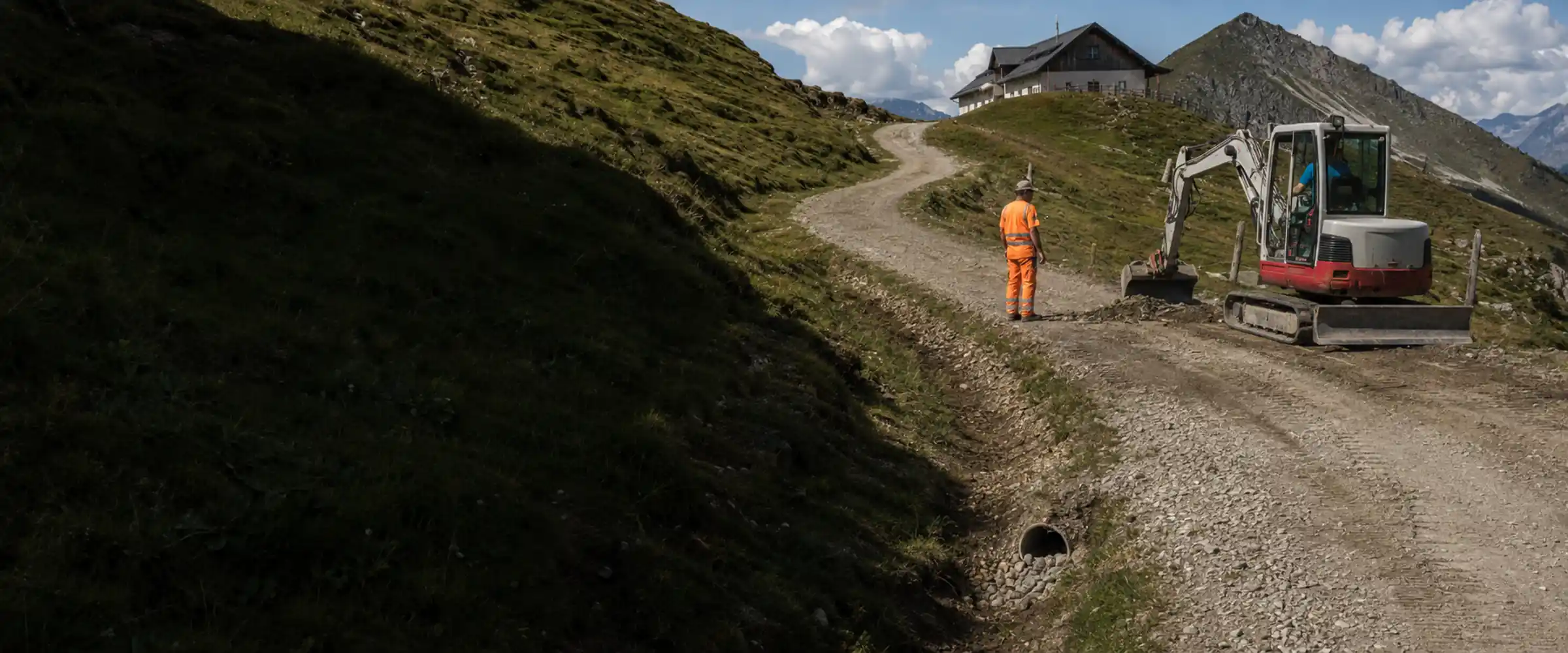 Path construction on the alpine pasture path: excavator and workers, water culvert in the foreground