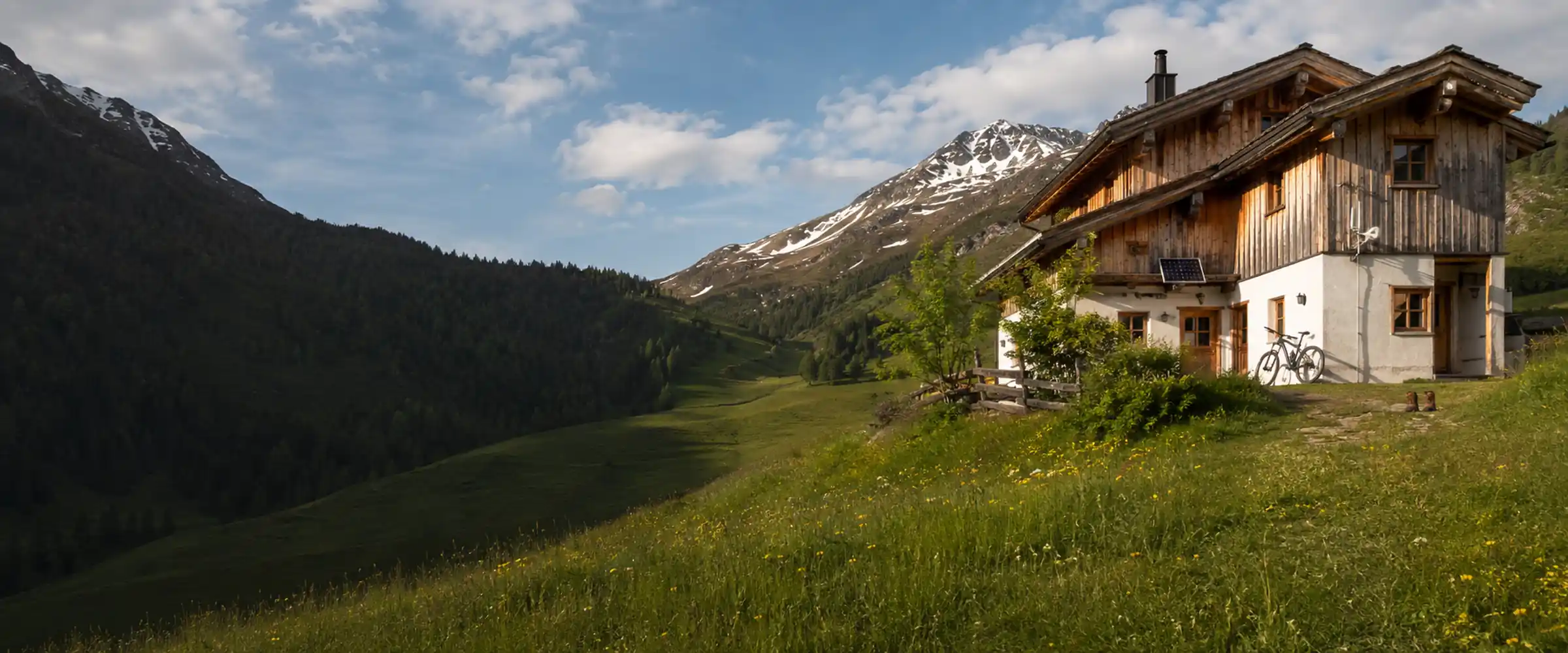 Alpine hut in early summer, remaining snow on the peaks and a blooming mountain meadow